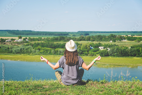 meditating girl in the hat on the bank of the river