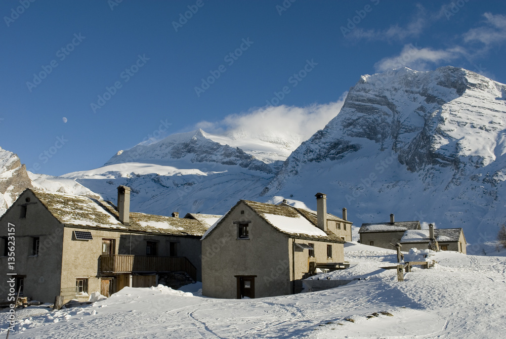 piccolo villaggio di baite in alta montagna, giornata di sole e nuvole dopo una nevicata, luna bianca, tramonto, inverno, alpi, Passo del Sempione, Svizzera