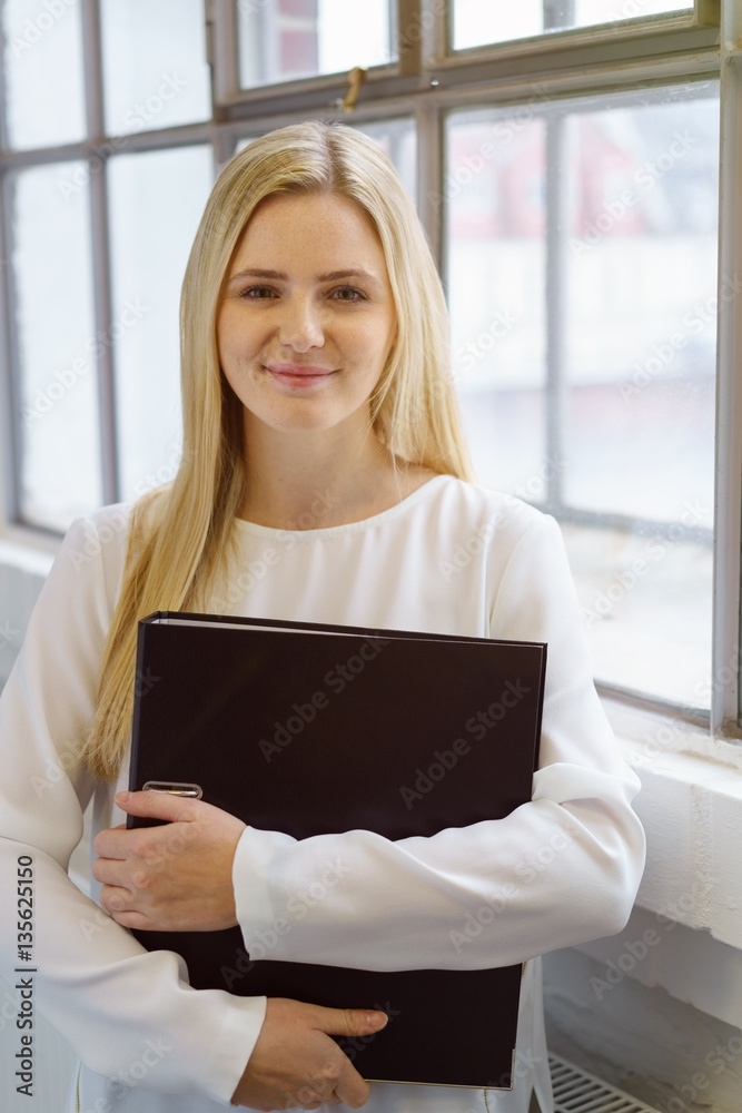junge blonde frau mit aktenordner am fenster junge blonde frau mit aktenordner am fenster