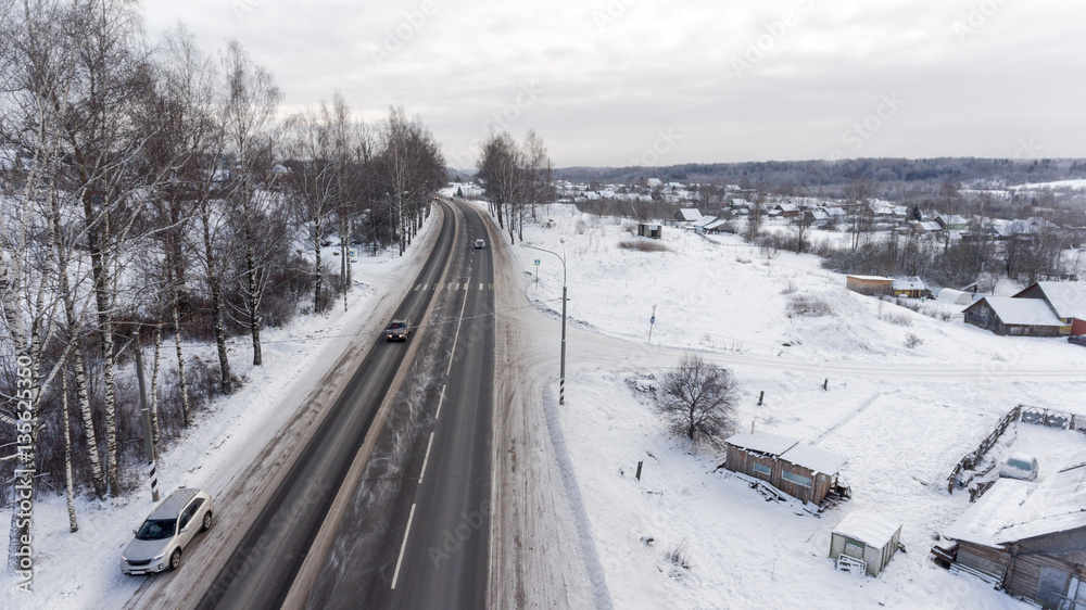 Snowy slippery federal three lane asphalt highway passing through the Russian village. Aerial view