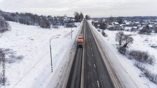Semitrailer trucks driving on winter three lane asphalt highway in village. Aerial view