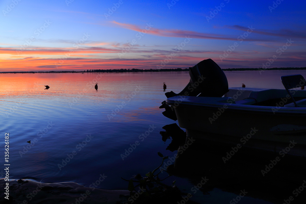 Beautiful sunset on the river parana in entre rios, Argentina, south america. A boat moored, the sky in orange and blue shades is reflected on the water of the river.