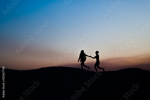 Young man and woman run together in love on a sunset. Silhouette