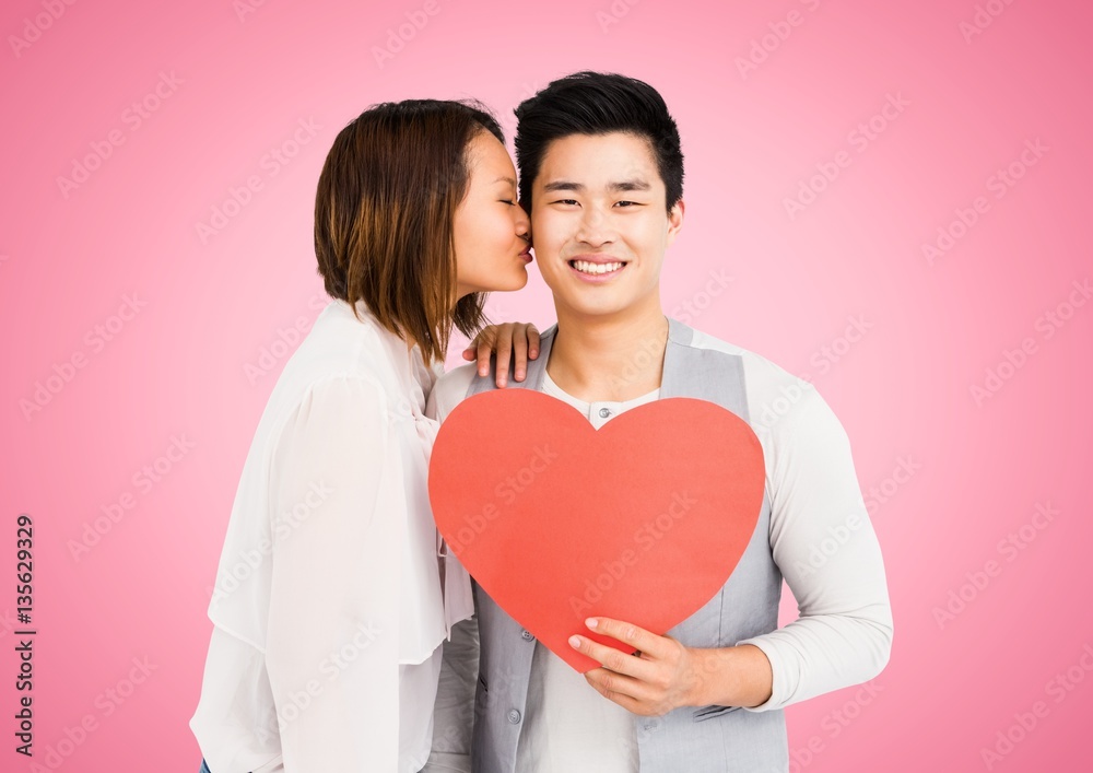 Woman kissing man while holding heart
