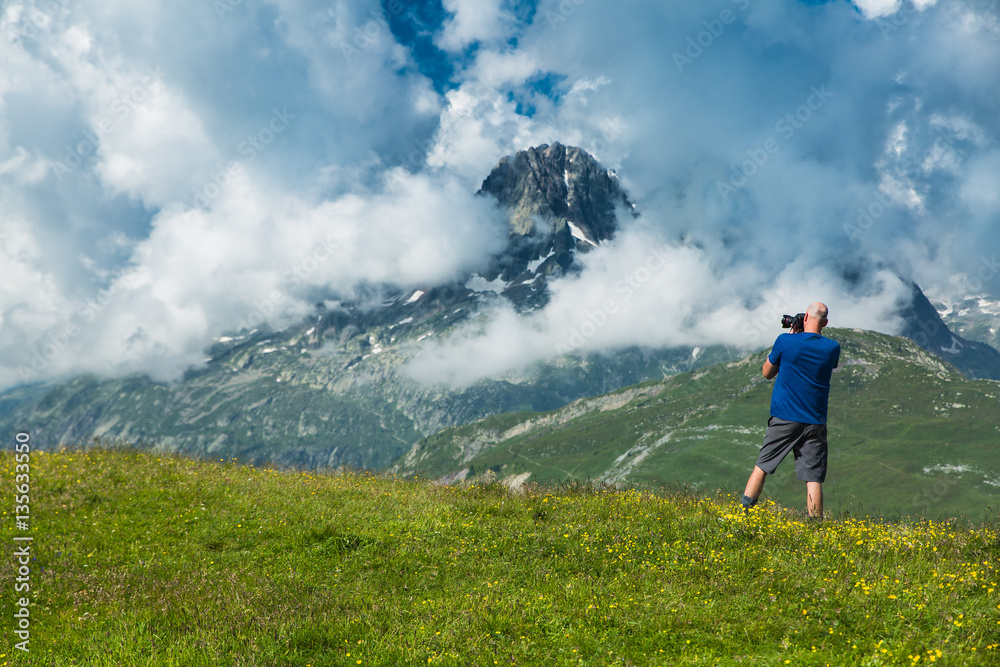 Φωτογραφία A tall bald man takes photos of the mountain valley and snow covered peaks of th