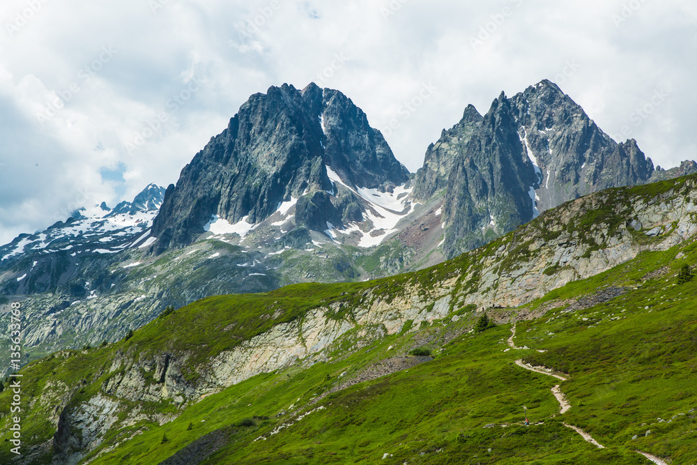 Boulder field and grassy meadows in the French Alps above Chamonix. Hiking trail crosses the foreground hill.
