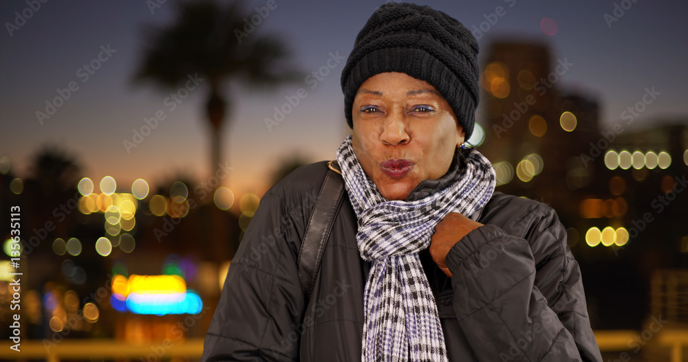 An older black woman in warm clothes downtown at night An older black woman in warm clothes downtown at night