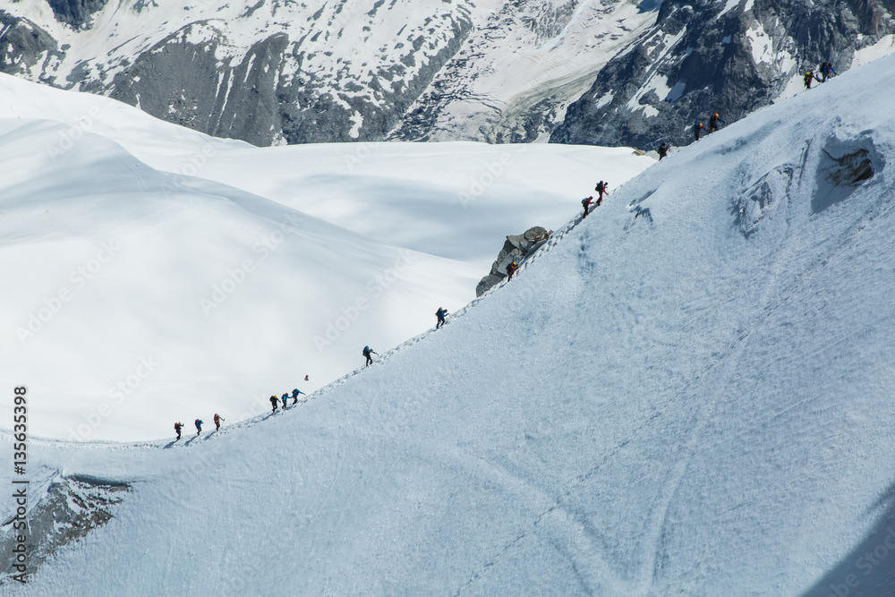 Mountaineers climb a long frozen ascent surrounded by ice and snow with a glacier in the background on Mont Blanc