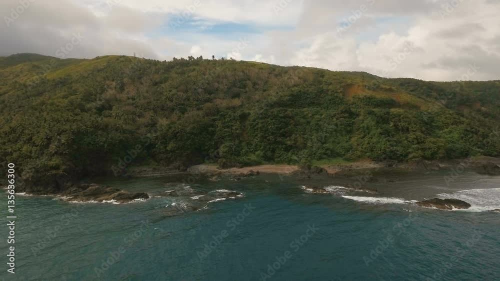 The coast of the tropical island with the mountains and the rainforest on a background of ocean with big waves.Aerial view: sea and the tropical island with rocks, beach and waves. Seascape: sky The coast of the tropical island with the mountains and the rainforest on a background of ocean with big waves.Aerial view: sea and the tropical island with rocks, beach and waves. Seascape: sky