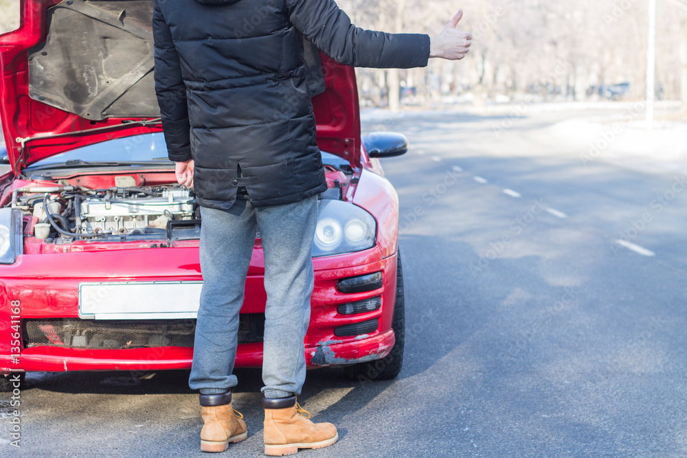 Obraz premium Mężczyzna sygnalizujący problemy z uszkodzonym sportowym samochodem na zimowej drodze.