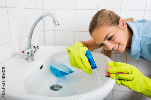 Smiling Woman Cleaning The Basin With Spray Bottle