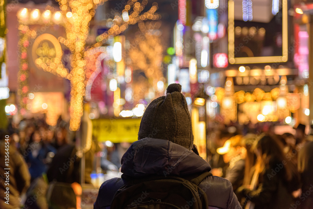 A man in front of a downtown street in Seoul lit by Christmas lights