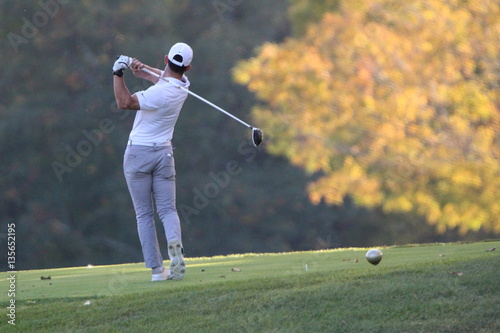 A muscular golfer tees off with his driver on an autumn day in New England with the Vermont foliage as bright as can be