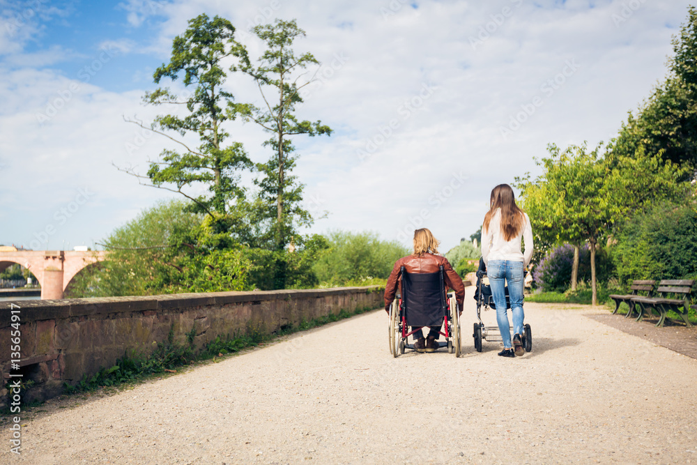 Young Parents In Wheelchair With Baby Stroller In The Park Young Parents In Wheelchair With Baby Stroller In The Park