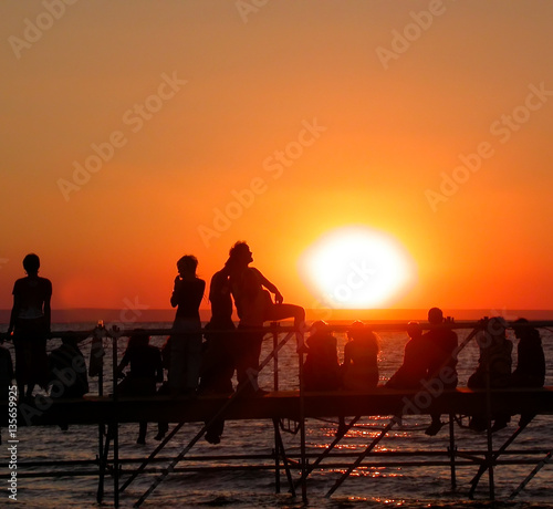 Group of young people on the ocean beach watching the sunset during beach party