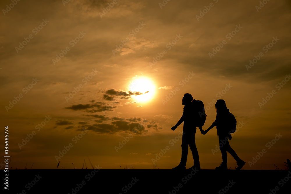 Silhouette of two backpackers (man and woman) who were traveling.The background image is a sunset in Thailand.Man and woman are walking hand in hand.