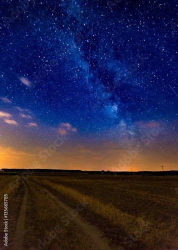Milky way over stubble field and rural sandy road
