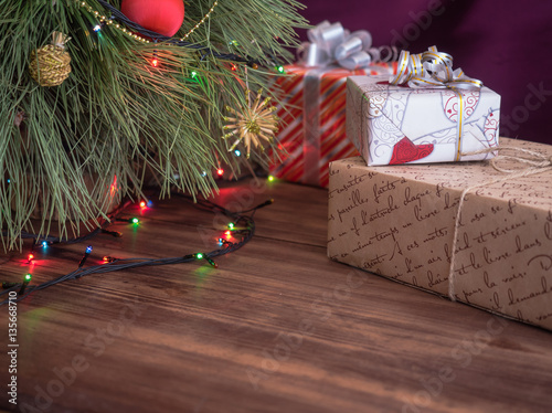 Green Christmas tree decorated with toys and garland with led lights. Boxes with gifts. Christmas present in boxes at wooden table. Green fir tree with toys and gifts under the tree.