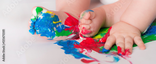 Baby child draws with colored paints hands, dirty feet.  Selective focus