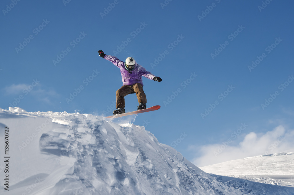 Stylish snowboarder with helmet and mask jumps from high snow slope Stylish snowboarder with helmet and mask jumps from high snow slope