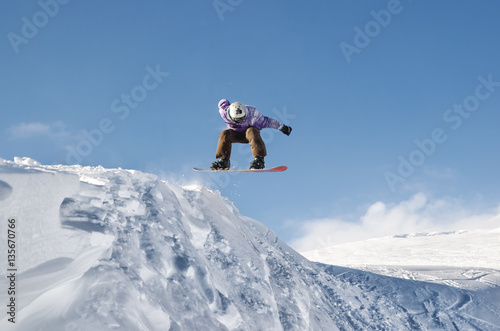 Stylish snowboarder with helmet and mask jumps from high snow slope