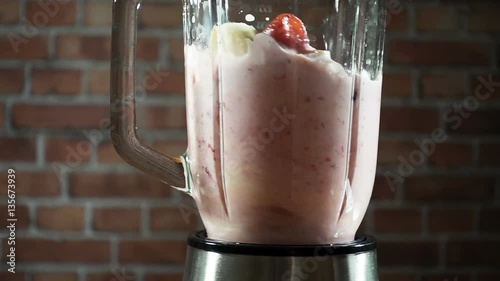 Blender with a banana strawberry milk smoothie on the kitchen, slow motion