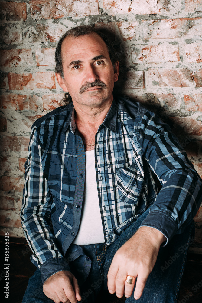 Handsome middle aged man is dressed in a casual clothing. Red brick wall background.