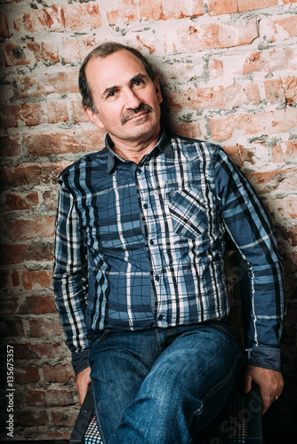 Handsome middle aged man is dressed in a casual clothing. Red brick wall background.