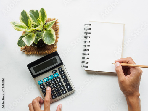 hand holding pancil writing on blank notebook and touch calculator