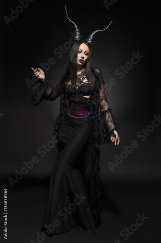 Young woman in black fantasy costume with big horns on dark background