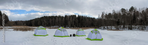 Tents on the ice against the background of the winter forest. Ice fishing.