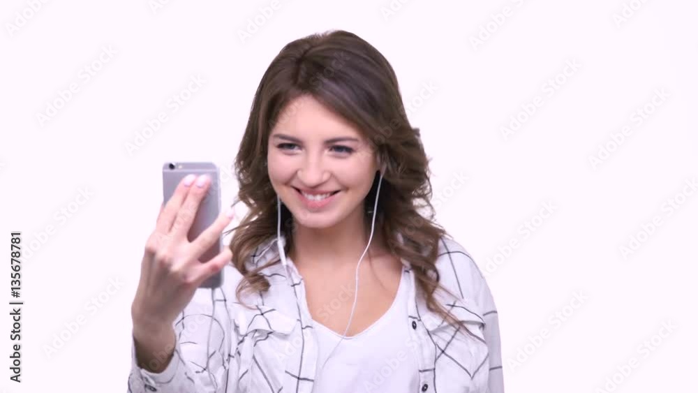 Smiling young woman waving hand during video call on mobile phone isolated on a white background Smiling young woman waving hand during video call on mobile phone isolated on a white background