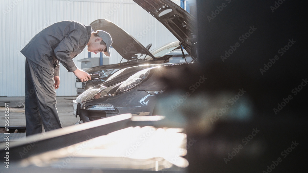 Mechanic in automobile garage checking hood for the luxury sport car