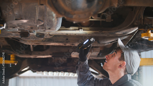 Mechanic is checking the bottom of car in garage automobile service, close up