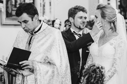 Lovely groom takes tears from bride's face while they stand behi photo