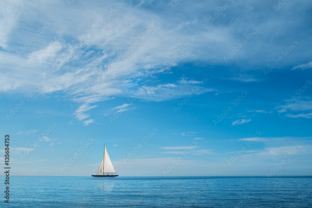 Obraz premium Sail boat on horizon at sea with blue sky and clouds