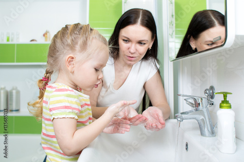 Child girl and mother washing hands with soap in bathroom