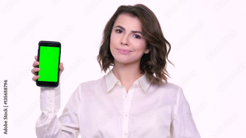 Happy beautiful young woman holding blank screen mobile phone and pointing finger over white background Happy beautiful young woman holding blank screen mobile phone and pointing finger over white background