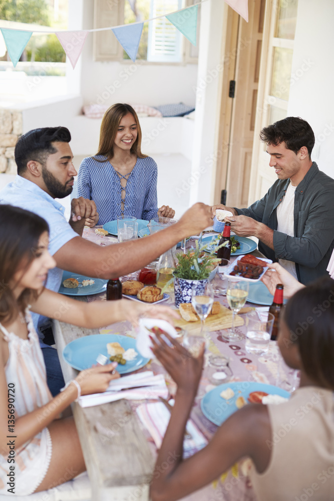 Friends serving each other at a dinner party on a patio Friends serving each other at a dinner party on a patio