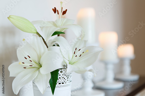 Fototapeta Naklejka Na Ścianę i Meble -  White lilies in a vase against a backdrop of candles. Flowers. Postcard