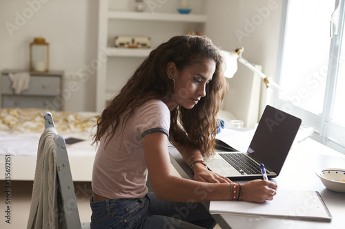 Teenage girl doing homework at a desk in her bedroom photo