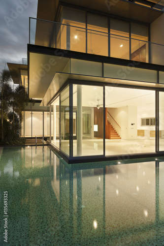 View into lit house with reflections in water of residential house 