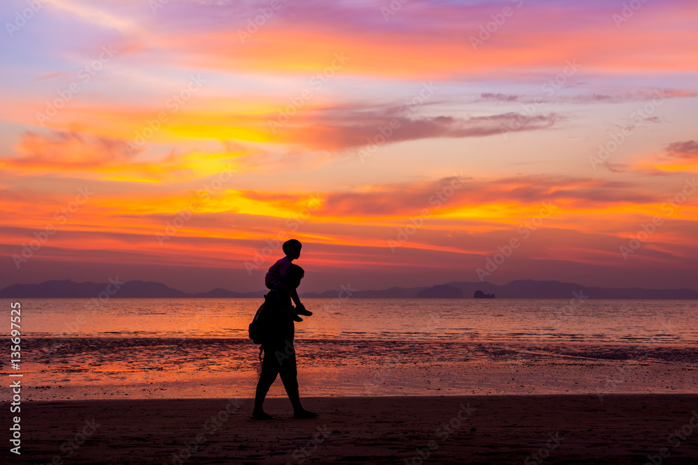 Father carrying his son on the neck walks on the beach at sunset over sea background. silhouette style