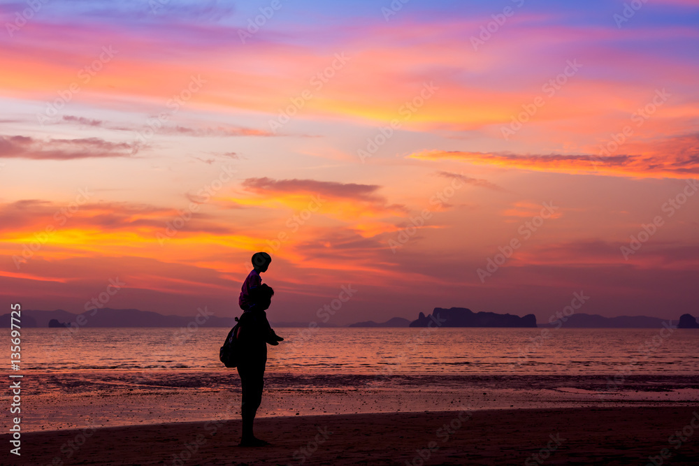 Father carrying his son on the neck walks on the beach at sunset over sea background. silhouette style