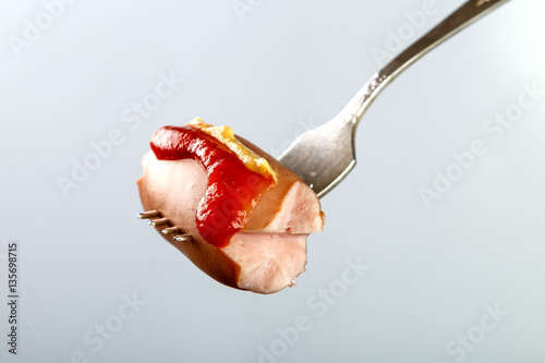 сосиска с кетчупом и горчицей на вилке
