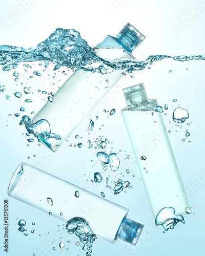 Three bottles of thermal water, cosmetic moisturizing lotion under the water. Big wave on the surface of water and many big and small bubbles in the water. Gradient blue background