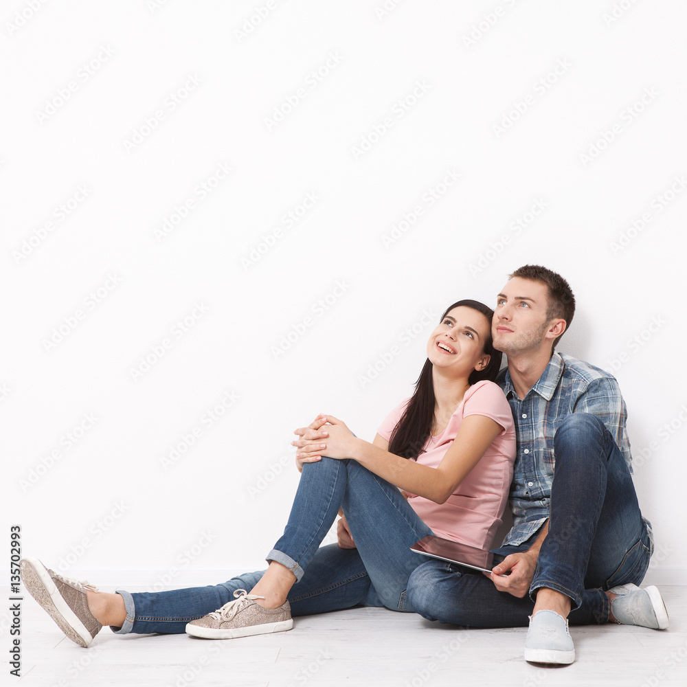 Happy young couple sitting on floor looking up while dreaming their new home and furnishing. Mock up. Happy young couple sitting on floor looking up while dreaming their new home and furnishing. Mock up.