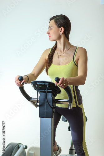 Young beautiful white girl in a yellow and gray sports suit is engaged on a stationary bike in the fitness club. © aleksandr_yu