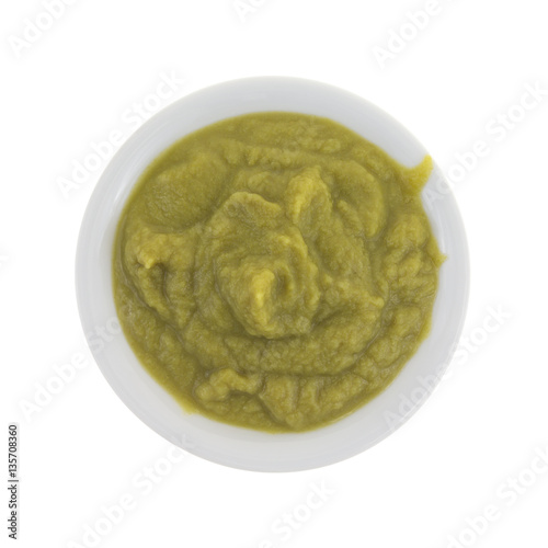 Green peas baby food mush in a bowl top view isolated on a white background.