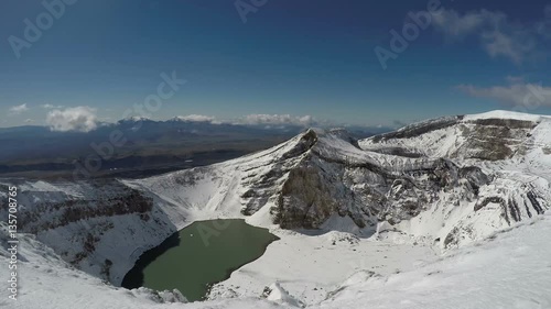 Volcanic landscape of Kamchatka Peninsula: beautiful view of snowbound craters and crater lake of active Gorely Volcano on a sunny day with dark blue sky. photo